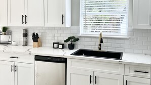 A modern kitchen with white cabinets, a marble countertop, a built-in dishwasher, and a window with blinds. - Charming 3BR/2BA Near Galleria/NRG, Top Hospitals & LA Fitness (Houston)