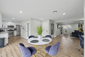 Una cocina moderna con armarios blancos, electrodomésticos de acero inoxidable y una zona de comedor con una mesa redonda y sillas moradas.