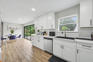 Een moderne keuken met witte kastjes, een vaatwasser en een raam met zonwering.