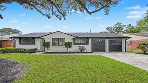 Une maison de plain-pied avec un garage, une pelouse bien entretenue et de grands arbres.