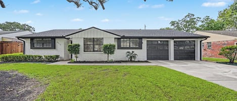 A single-story house with a garage, a well-maintained lawn, and mature trees.