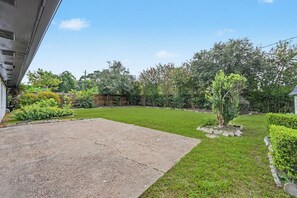 Een achtertuin met gazon, een kleine boom en een betonnen terras.