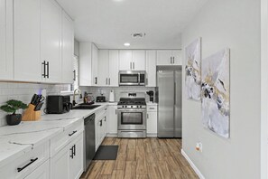 Une cuisine moderne avec des armoires blanches, des appareils en acier inoxydable et un plancher en bois.