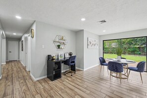 Een modern interieur met een eethoek, een werkplek met bureau en stoelen, en uitzicht op een tuin door grote ramen.