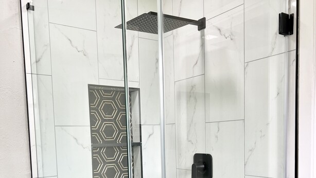 Une salle de bain moderne avec une douche à parois de verre, des carreaux de marbre blanc et un mur orné d’un motif géométrique.