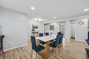 A modern dining area with a white table and dark chairs, wooden flooring, and artwork on the walls.