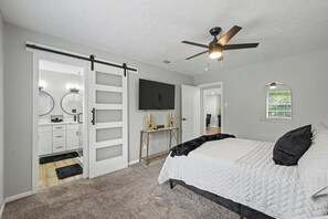 Een slaapkamer met een bed, een plafondventilator, een televisie en een schuifdeur naar een badkamer.
