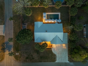 Une vue aérienne d’une maison avec une piscine, une terrasse dotée de parasols et un grand arbre.