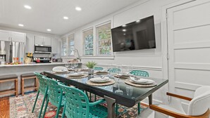 Een eetgedeelte met een glazen tafel, teal stoelen en een kamerbreed tapijt met een patroon.