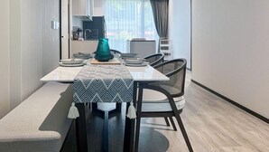 Un espace de salle à manger moderne avec une table dressée pour quatre personnes, un vase turquoise et une cuisine en arrière-plan.
