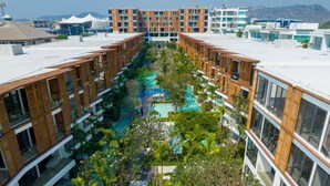 Un hôtel moderne doté d’une cour intérieure où se trouve une piscine, le tout entouré d’immeubles à plusieurs étages, caractérisés par de grandes fenêtres et des éléments décoratifs en bois.
