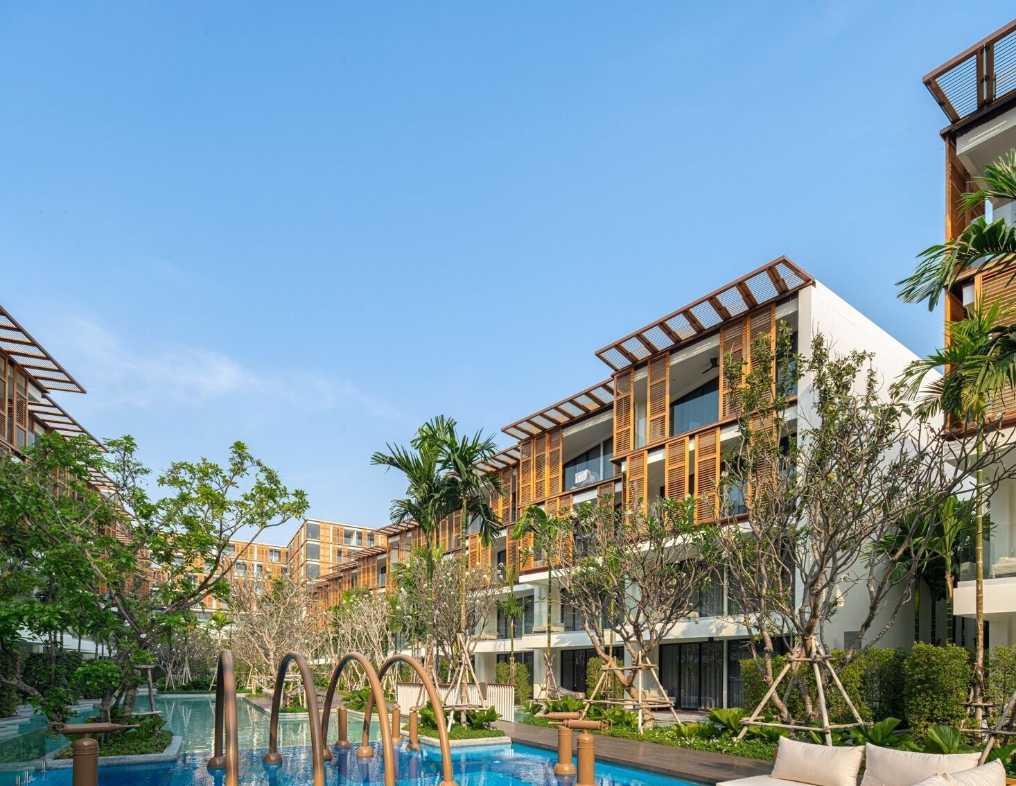 Un hotel moderno con varios balcones, piscina y abundante vegetación.