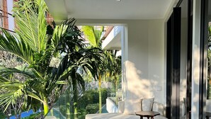 Un balcon moderne doté d’un canapé, d’une petite table et d’une rambarde en verre, offrant une vue sur un jardin et des immeubles.