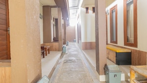 A narrow hallway with benches, trash bins, and a bench with a yellow cushion. - Asri Guesthouse (Aik Berik)