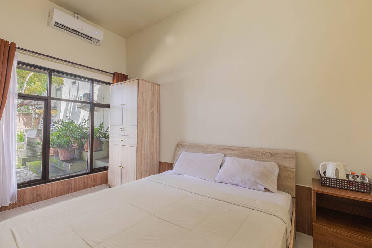 Een hotelkamer met een bed, een kledingkast, een raam met gordijnen en een klein tafeltje met waterkoker en dienblad.