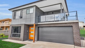 A modern two-story house with a garage, a balcony, and a large window. - Heather - Pet Friendly Merimbula (Merimbula)