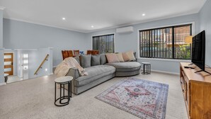A modern living room with a grey sectional sofa, a small round table, a patterned rug, and a TV on a wooden cabinet. - Heather - Pet Friendly Merimbula (Merimbula)