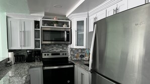 A compact kitchen with stainless steel appliances, white cabinets, and a granite countertop. - SEAFLECTIONS - Relax, Reflect & Reminisce on the MUSIC, ART and CULTURE.  (Kingston)