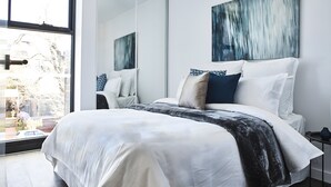 A modern bedroom with a large bed, a mirror, and a painting on the wall. - Mega Style Apartments - The Marc (St Kilda)