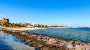 A coastal cityscape with a rocky shoreline, buildings, and a clear blue sky. - Mega Style Apartments - The Marc (St Kilda)