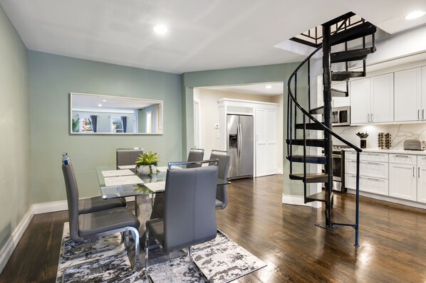 A modern kitchen with white cabinets, a stainless steel refrigerator, and a black spiral staircase.