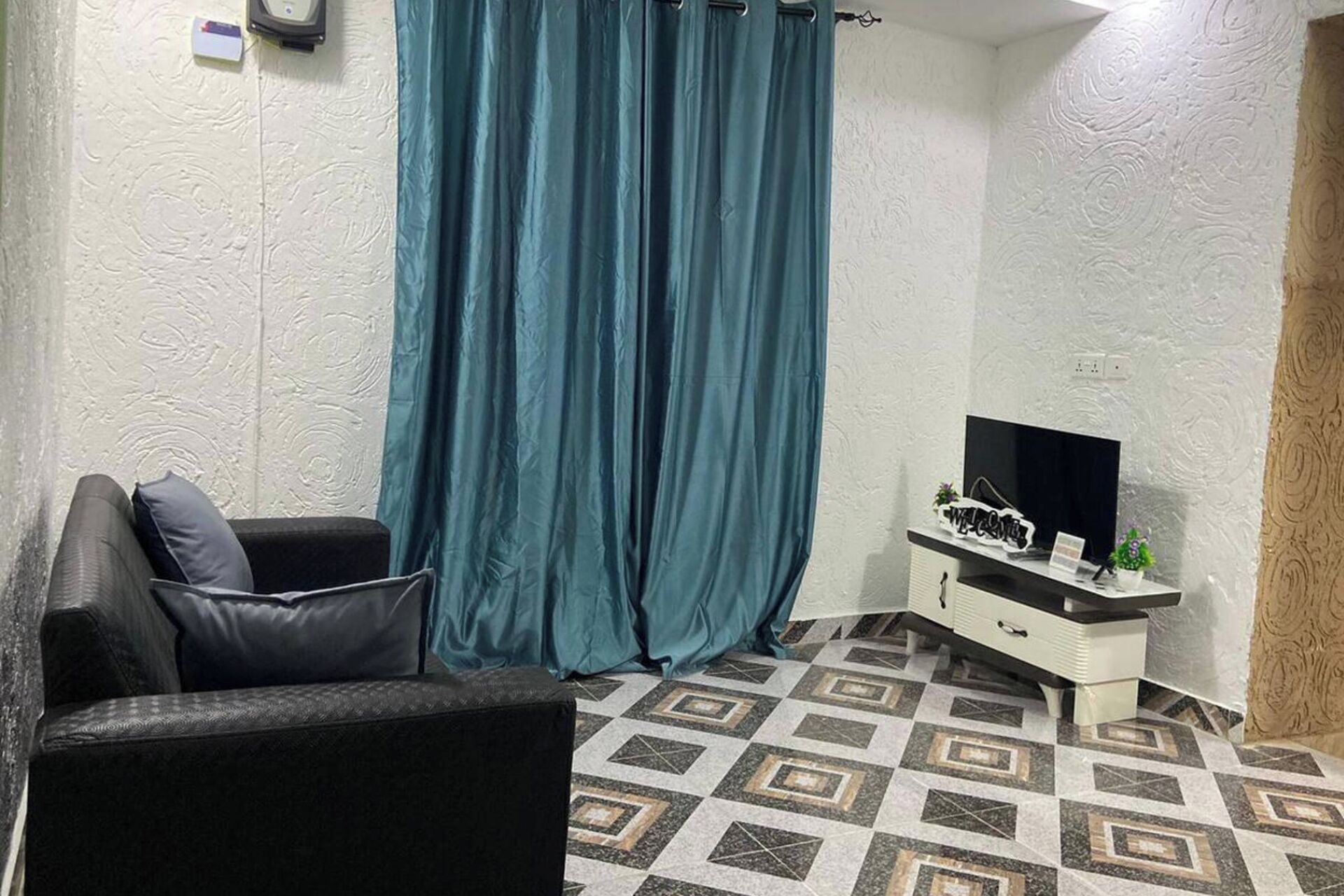 A room with a sofa, a TV on a white cabinet, and patterned flooring.