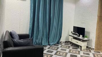A room with a sofa, a TV on a white cabinet, and patterned flooring.