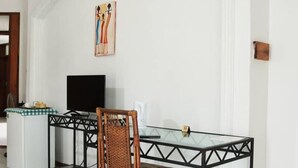 Un comedor con una mesa de vidrio, una silla de mimbre, un refrigerador blanco y un televisor negro sobre un mueble.