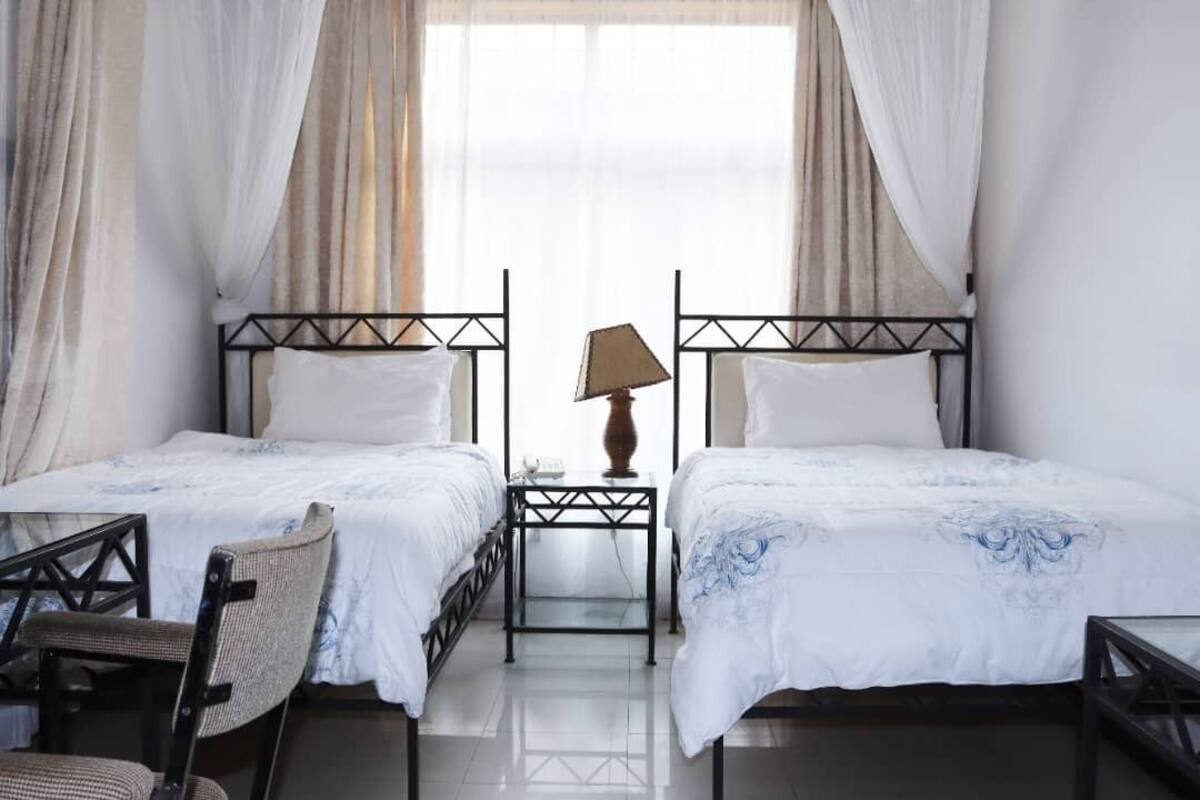 Una habitación de hotel con dos camas, una mesita de noche, una silla y una ventana con cortinas.
