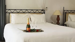 Una habitación de hotel con una cama, una mesita de noche con una lámpara y una botella de champán sobre la cama.