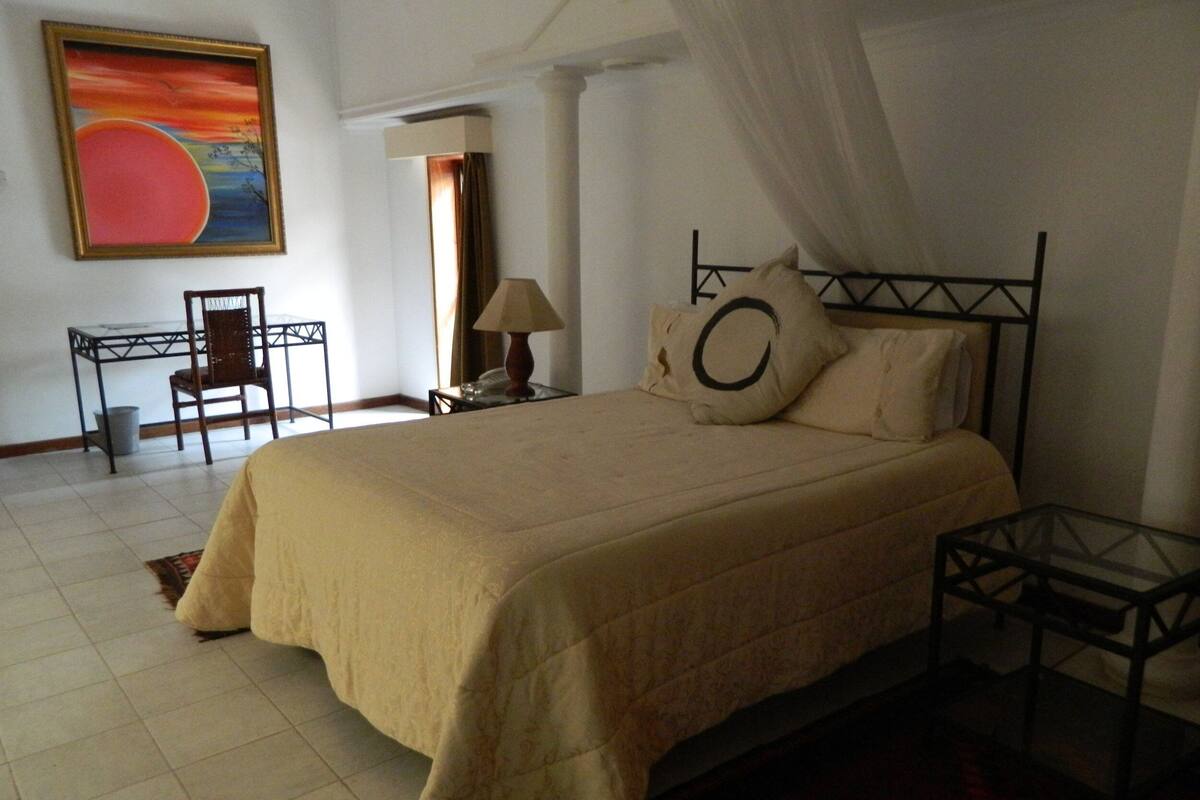 Un dormitorio con una cama grande, una mesita de noche, una silla, una lámpara y un cuadro en la pared.