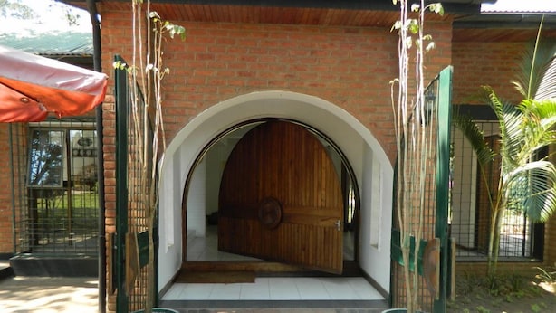 Un edificio de ladrillo con una puerta de madera grande y un acceso abovedado. Hay dos macetas con plantas a cada lado de la puerta.