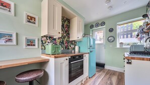 A kitchen with wooden countertops, a green refrigerator, and a wall with framed pictures.