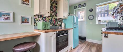 A kitchen with wooden countertops, a green refrigerator, and a wall with framed pictures.