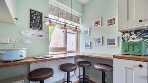 A kitchen with a wooden countertop, bar stools, a window with curtains, a wall-mounted sign, and a radiator.
