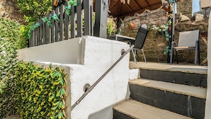 A set of outdoor stone steps leading to a covered area with a wooden fence and greenery.
