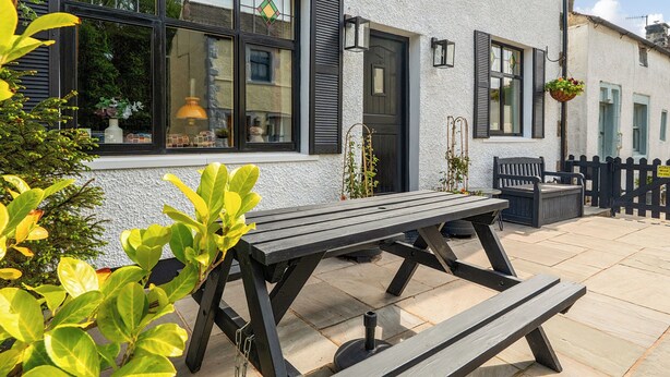 A patio with a wooden table and benches, a white building with black shutters, and a black fence.