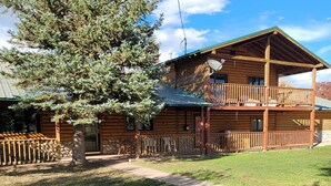 A wooden cabin with a balcony, a stone foundation, and a well-maintained lawn. - Grandote Lodge (La Veta)