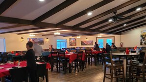 A restaurant with wooden flooring, tables with red tablecloths, and a high ceiling with exposed beams. - Grandote Lodge (La Veta)