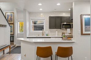 A modern kitchen with a white countertop, two brown chairs, a stainless steel microwave, and a hexagonal patterned backsplash. - Hot Tub, Skiing 2 Min Away, Cozy Modern Condo! (Durango)