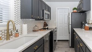 Una cocina moderna con armarios oscuros, encimera blanca y salpicadero de azulejos hexagonales.