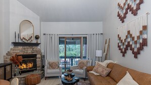 Sala de estar con chimenea de piedra, dos sillones, un sofá y una mesa de centro. Se ve un paisaje al exterior a través de un ventanal.