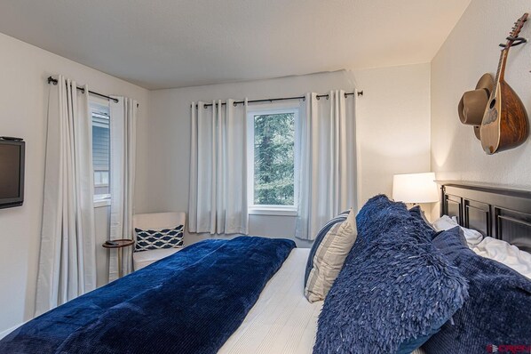 A bedroom with a bed, a chair, a guitar, and a window with curtains. - Hot Tub, Fishing/Hiking Close, 30 Min to Silverton! (Durango)