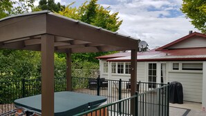 A covered outdoor area with a hot tub, a fenced patio, and a house in the background.