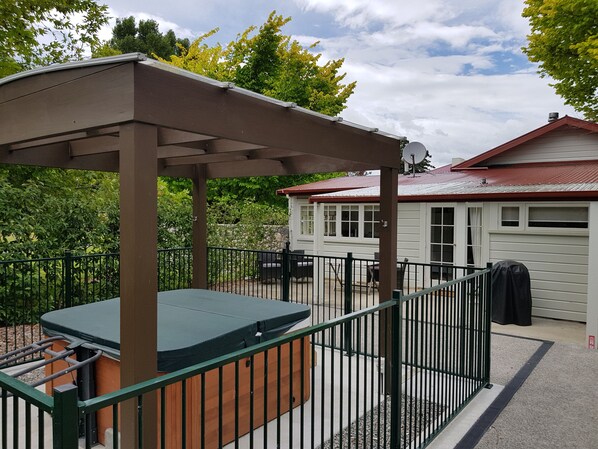 Een overdekt buitengebied met een hottub, een omheind terras en een huis op de achtergrond.