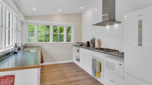 A modern kitchen with a large window, white cabinetry, and a stainless steel range hood.