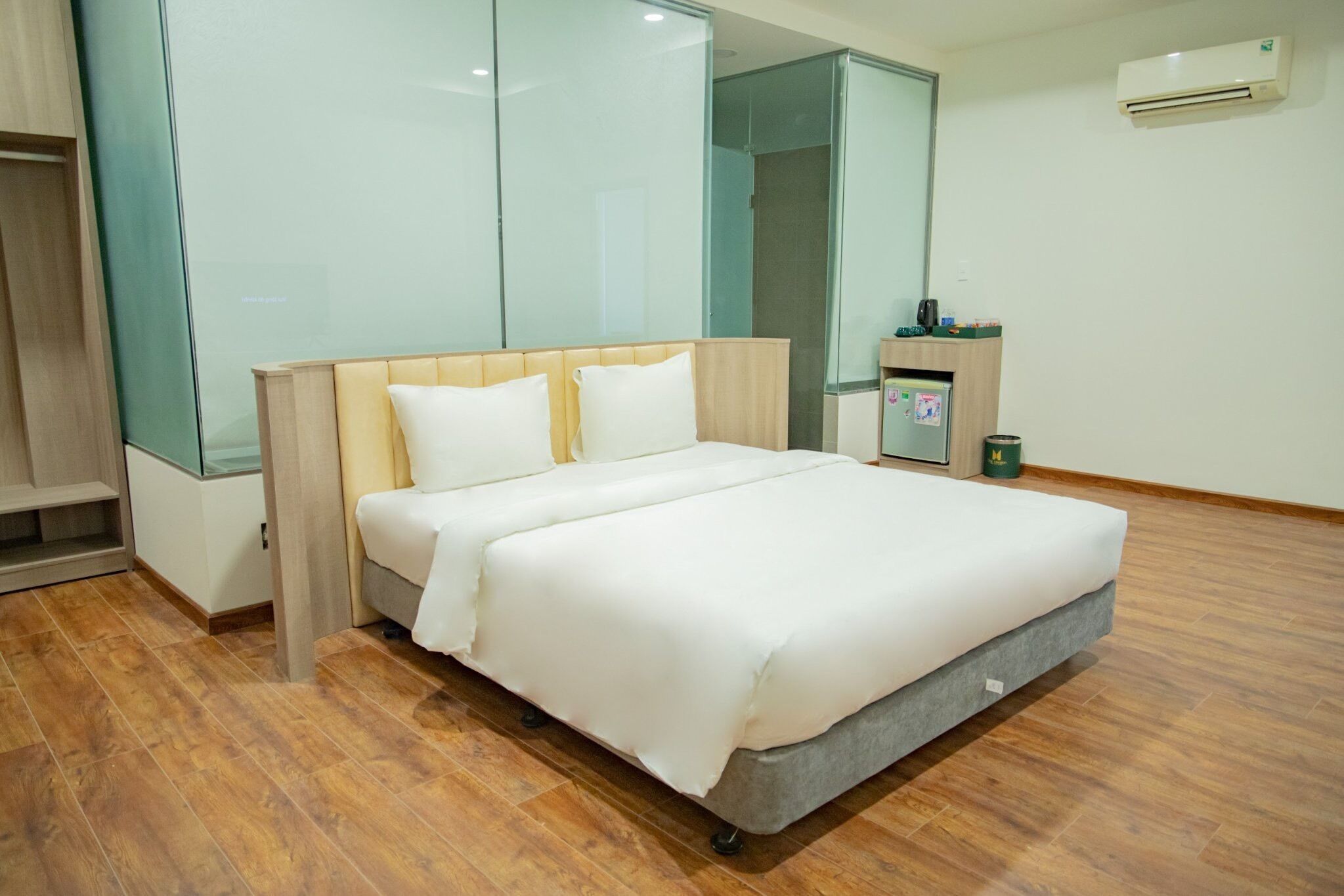 A modern hotel room with a large bed, a small desk, and a glass partition wall.