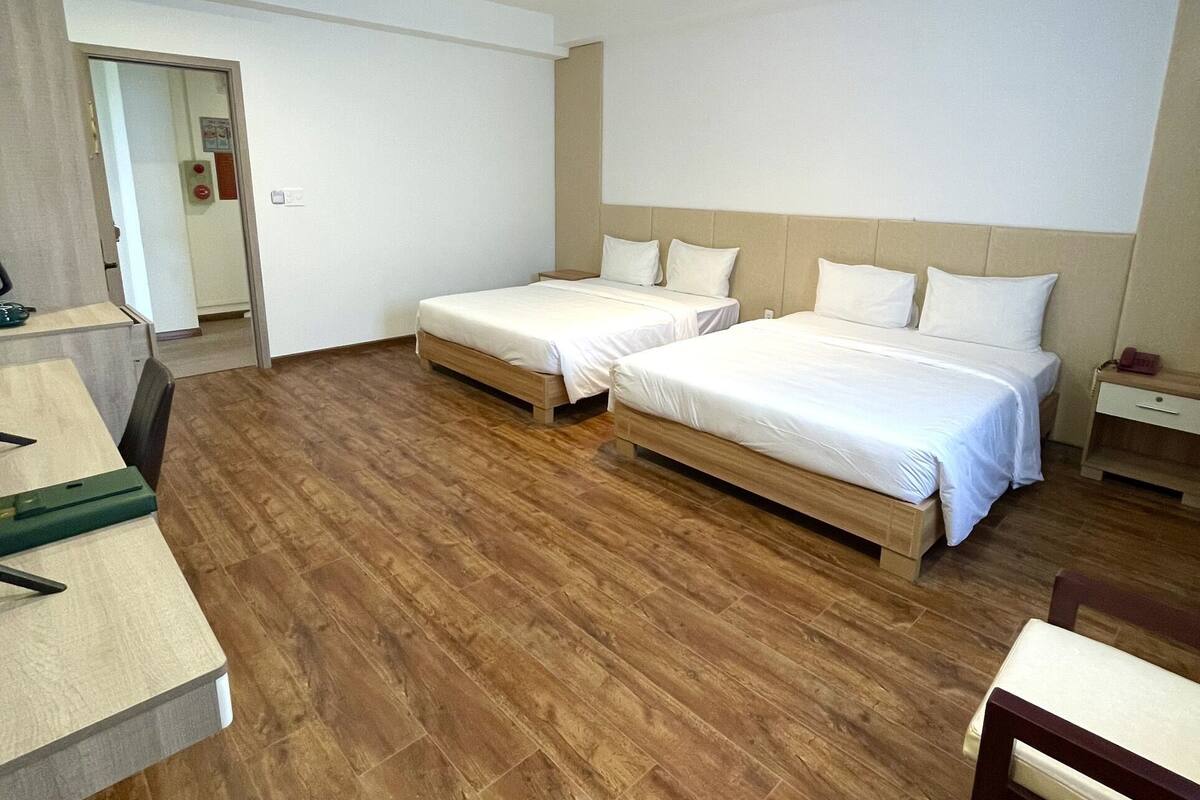 Une chambre d’hôtel avec deux lits simples, un plancher en bois, un bureau et une chaise.