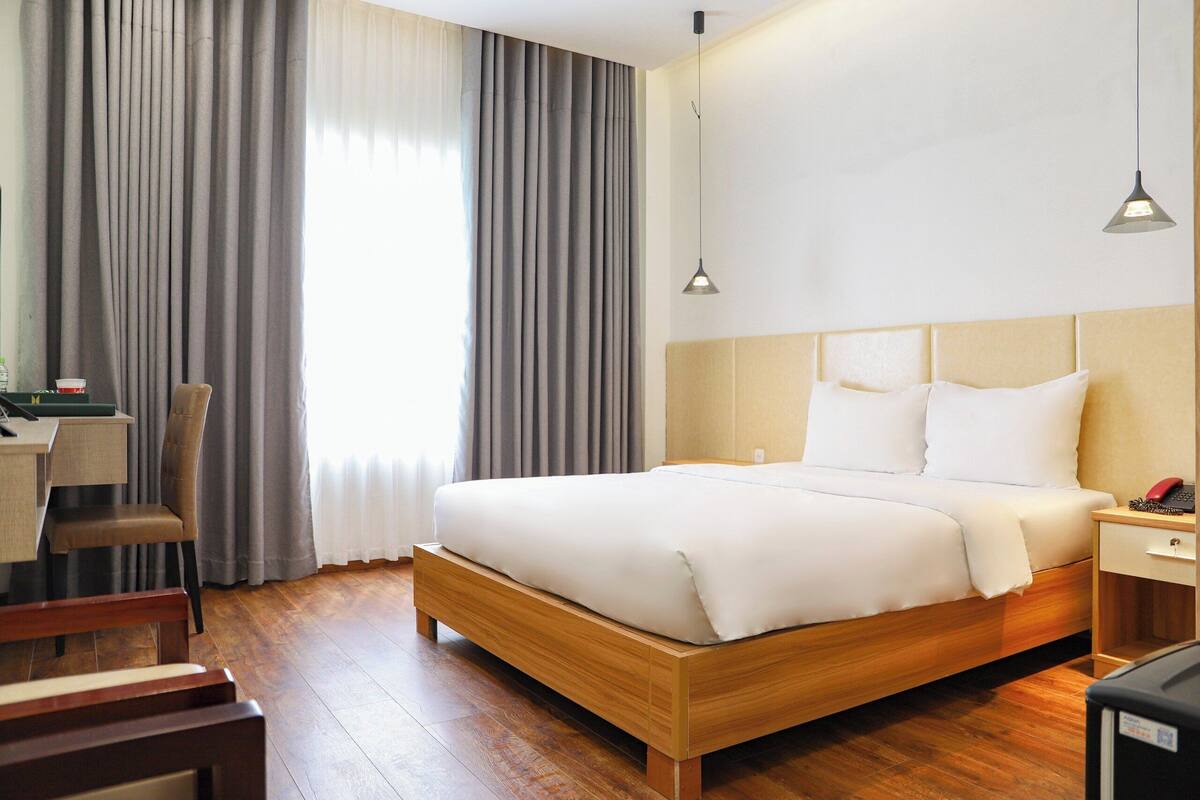 Une chambre d’hôtel avec un lit en bois, un bureau avec une chaise, une table de chevet et une lampe.