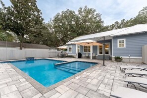 A backyard with a swimming pool, patio furniture, and a covered seating area.
